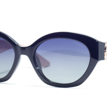 "Guess GU 00104 05D sunglasses with large oval black frames, blue gradient lenses, and a distinctive pale pink temple with a decorative gold logo."